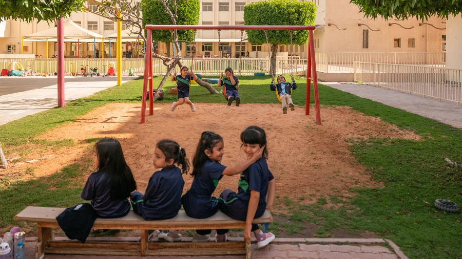 Elementary students sitting on bench and swinging on swing set