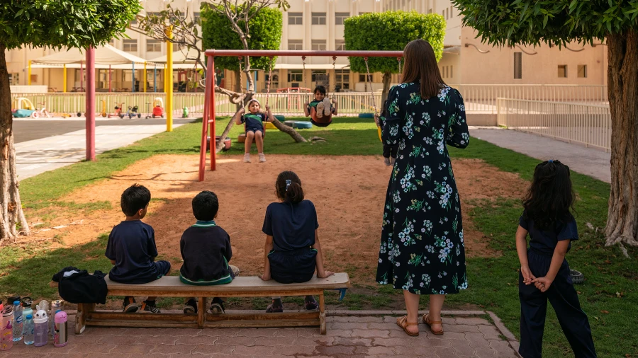 Students playing on playground, teacher watching